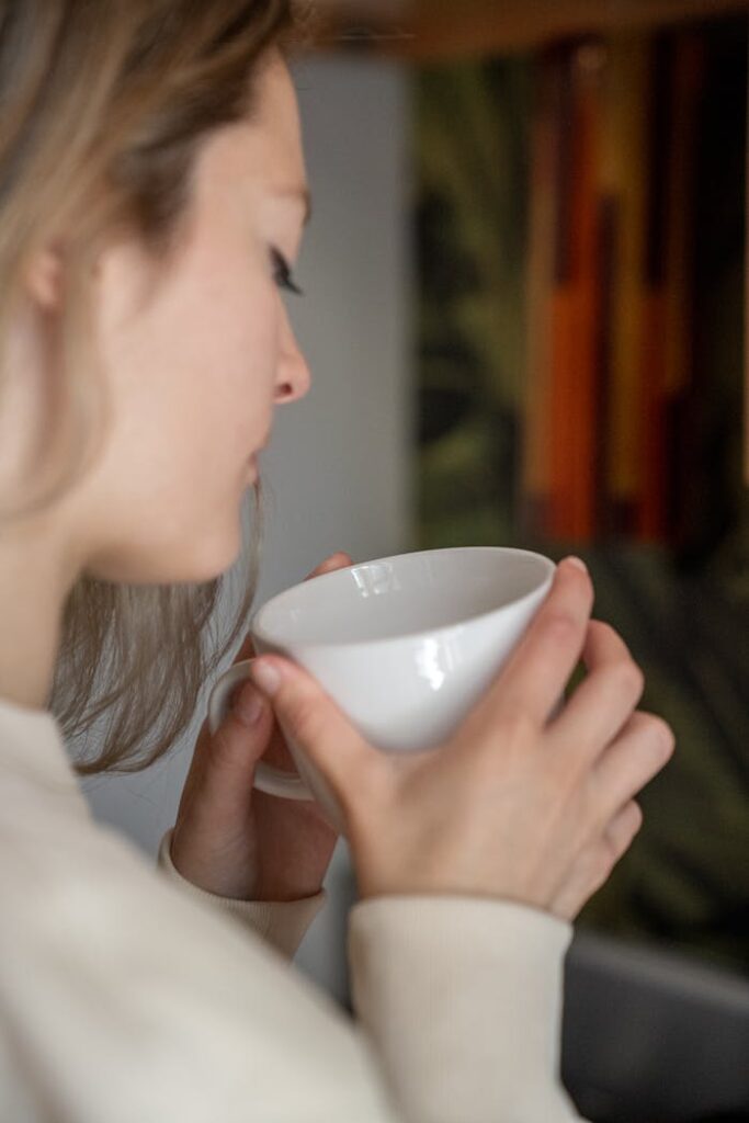 Side profile of a woman holding a white mug, enjoying a hot drink indoors. Warm and cozy atmosphere.
